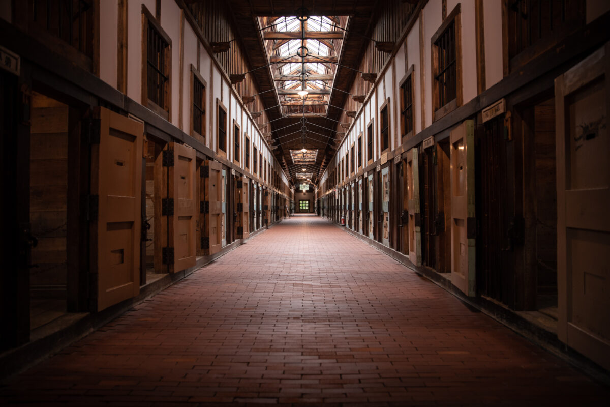 Symmetrical Abashiri Prison corridor with brick floor, wooden cell doors, and skylights