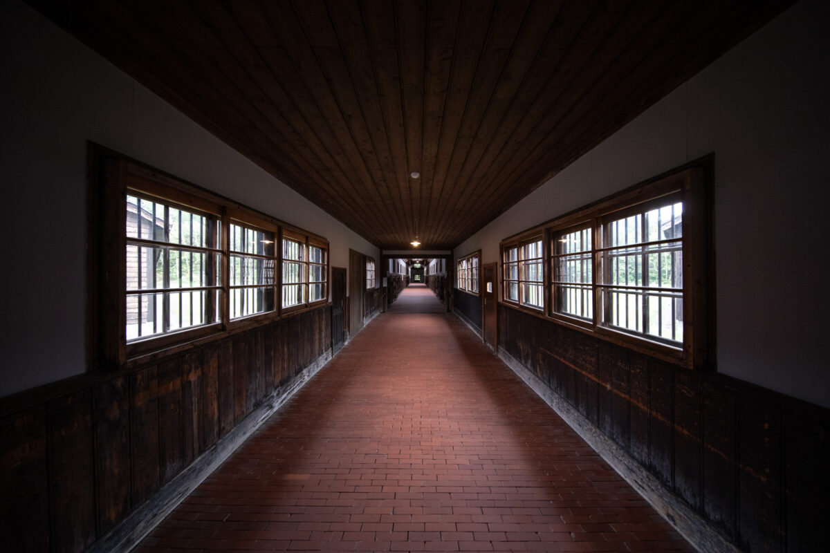 Symmetrical Abashiri Prison corridor with barred windows, dark wood walls, and red brick floor.