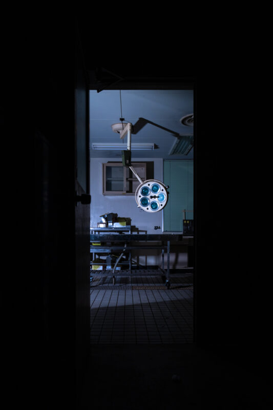 View through dark hallway into sterile animal research lab operating room with exam table and surgical light.