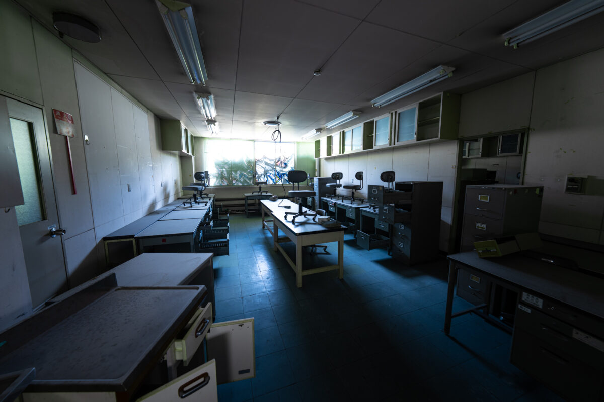Abandoned animal research lab with workbenches and equipment, lit by sun through window.