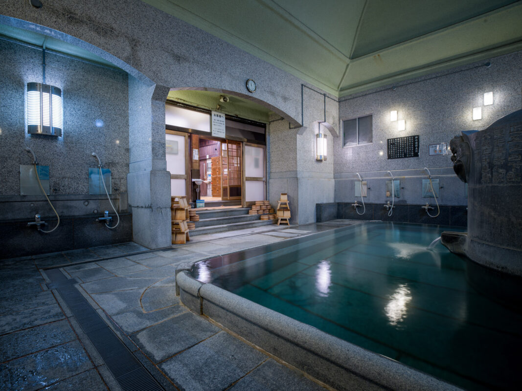 Serene Dōgo Onsen bathhouse interior with stone soaking pool and traditional wash stations