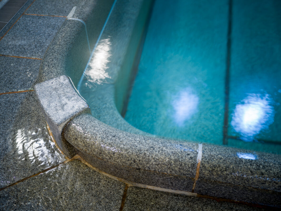 Turquoise onsen bath with granite rim and gentle waterfall at Dogo Onsen