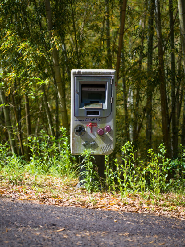Game Boy-shaped mailbox on a wooded trail, retro Nintendo design with magenta buttons