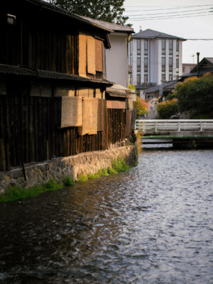 Kyoto Gion canal with traditional wooden houses, bamboo blinds, and bridge reflections.