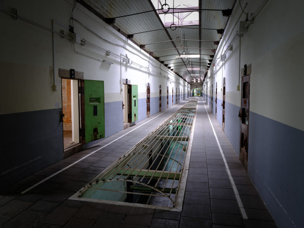 Empty corridor in historic Nara Prison cellblock with green cell doors and grated drain
