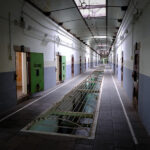 Empty corridor in historic Nara Prison cellblock with green cell doors and grated drain