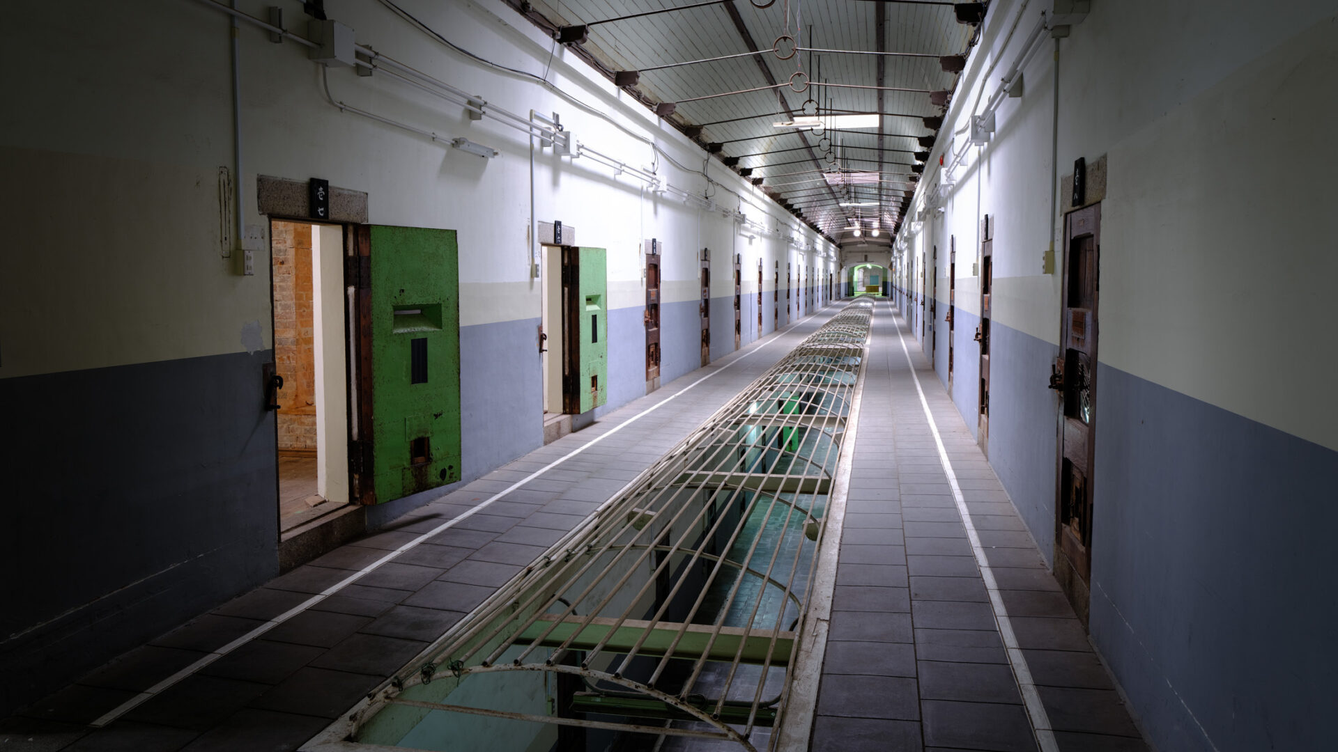 Empty corridor in historic Nara Prison cellblock with green cell doors and grated drain