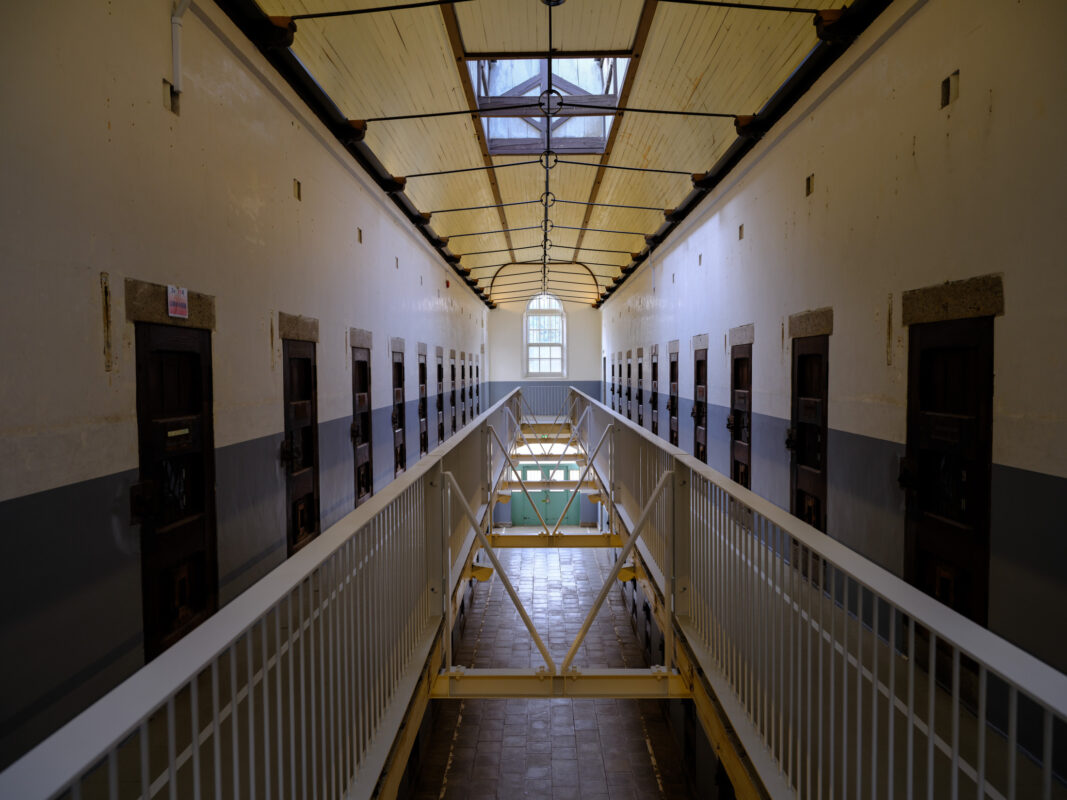 Symmetrical corridor in historic Nara Prison with cell doors, walkway, yellow railings, and skylight.