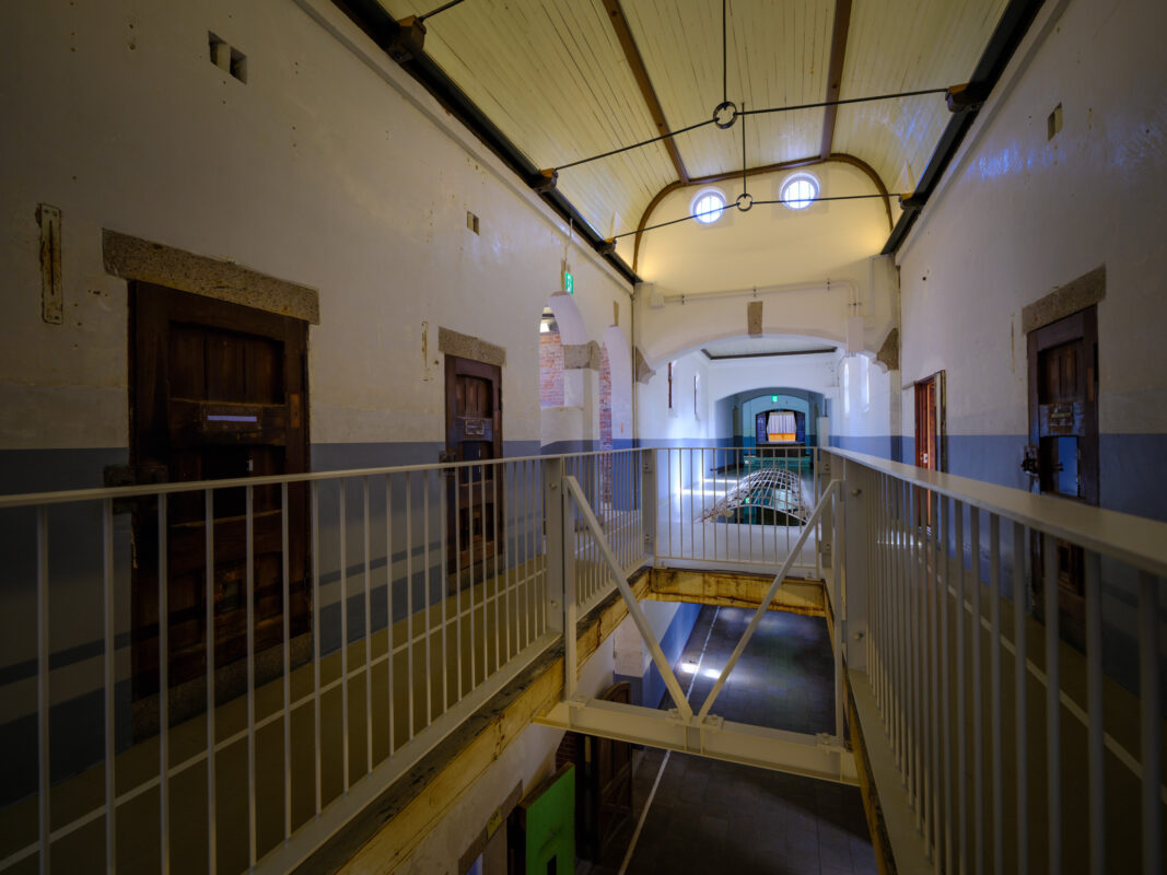 Symmetrical corridor inside historic Nara Prison with cell doors and railings, daylight overhead.