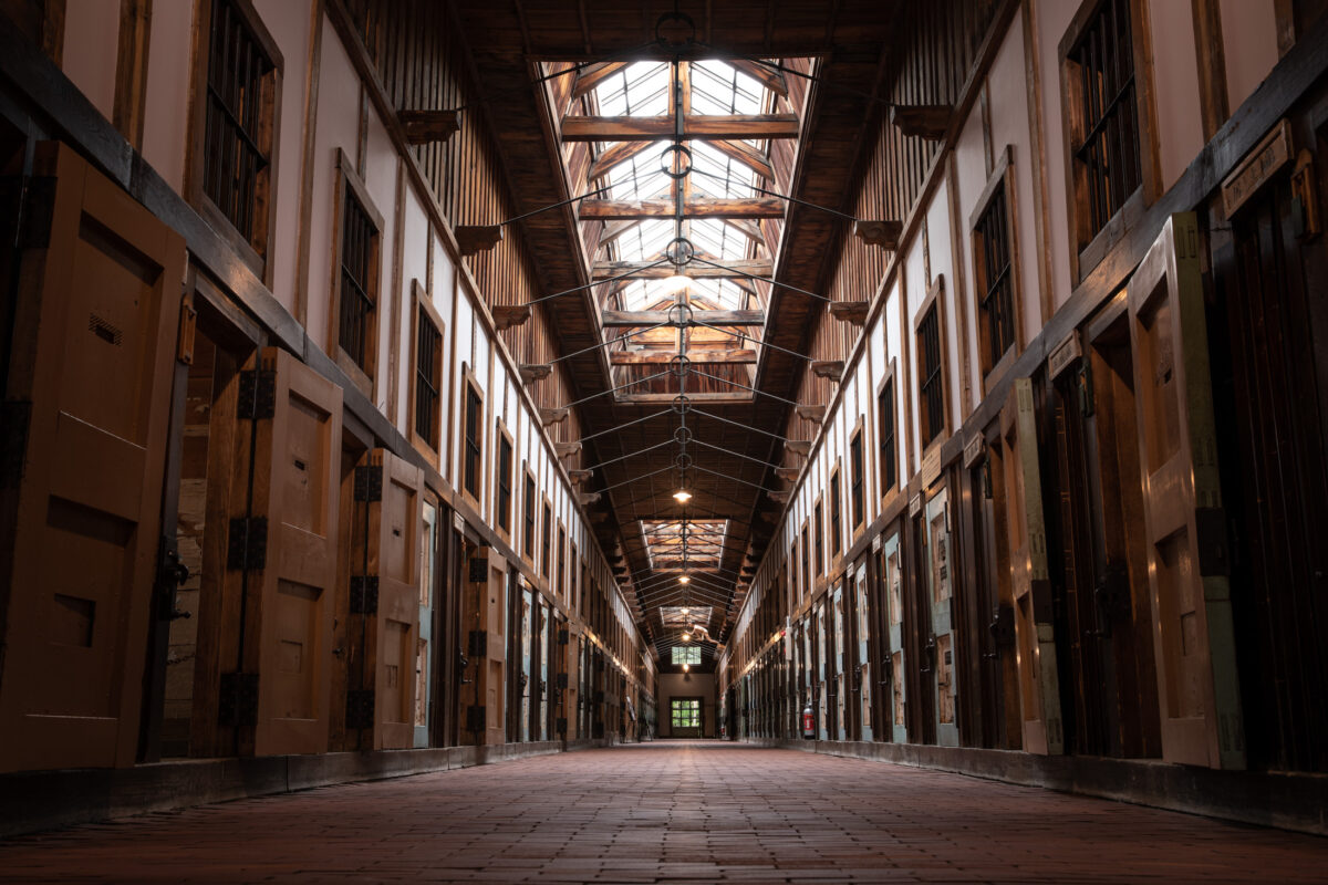 Symmetrical Abashiri Prison cellblock corridor with wooden cell doors, iron bars, and skylights