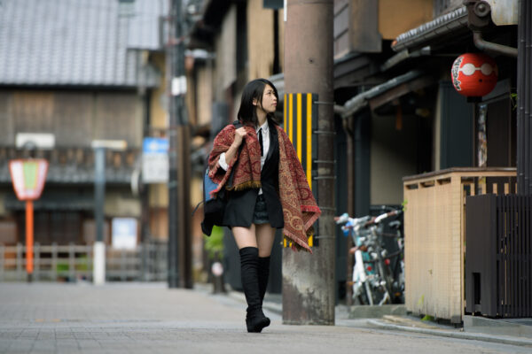 Woman in modern kimono jacket and boots walking a narrow Kyoto street by red lantern
