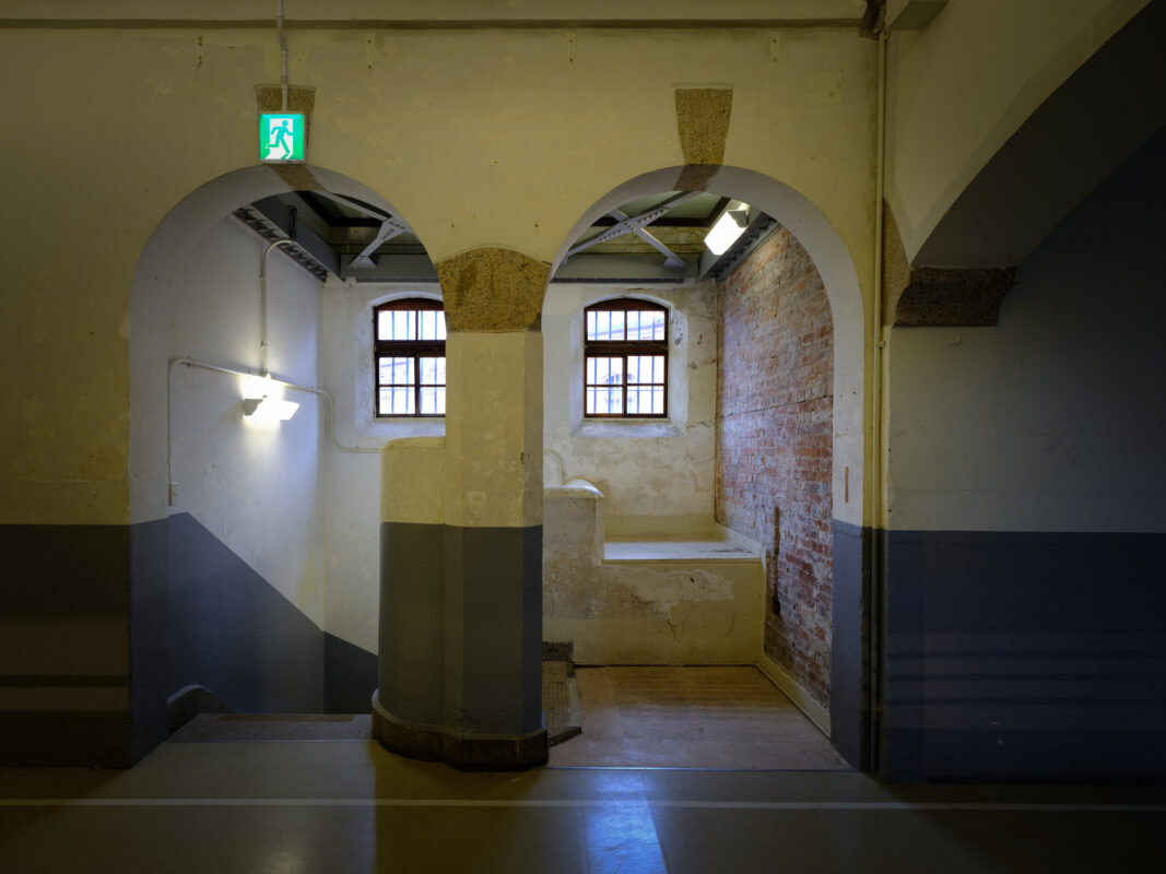 Empty arched corridor inside historic Nara Prison with barred windows and exposed brick.