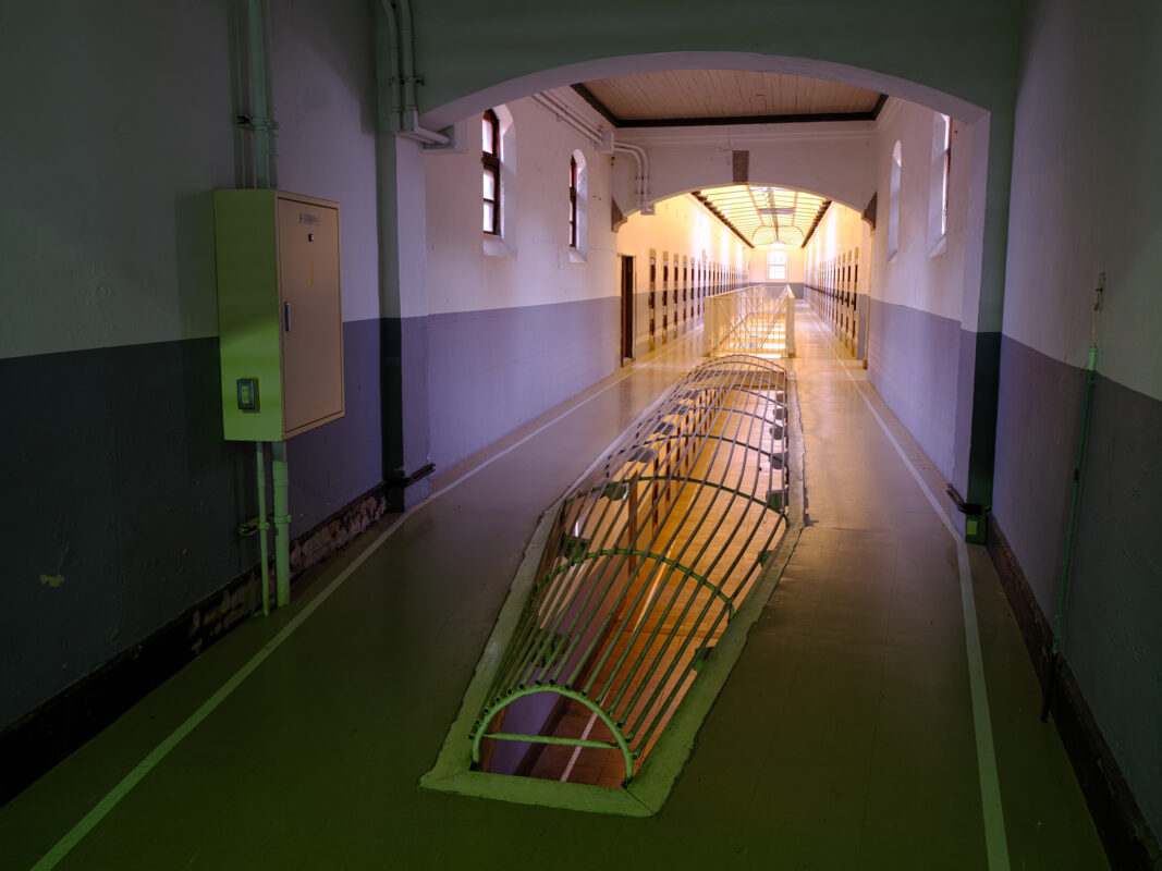 Arched corridor inside Nara Prison with barred floor structure leading to bright exit.