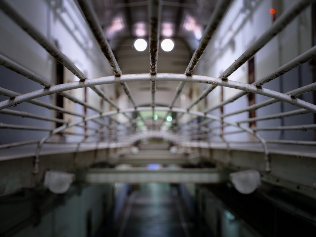 Symmetrical barred corridor inside historic Nara Prison with arched metal bars and cool lights.
