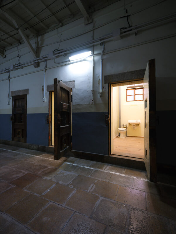Historic Nara Prison corridor with open cell doors and lit cell showing toilet and sink.