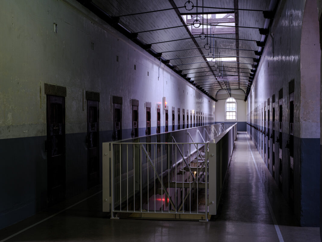 Symmetrical Nara Prison cellblock corridor with metal doors, arched skylight, and gated stairwell