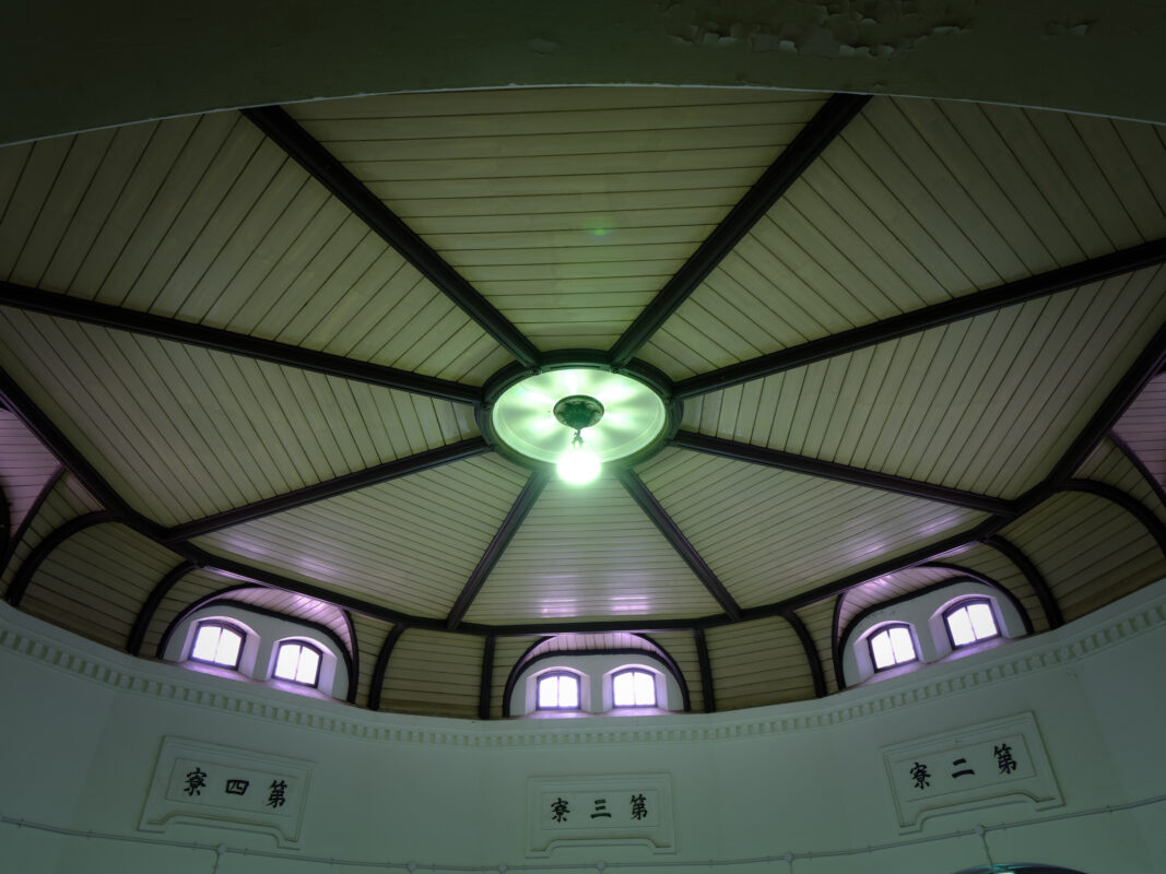 Upward view of Nara Prison interior dome ceiling with radial beams, central light, arched windows.