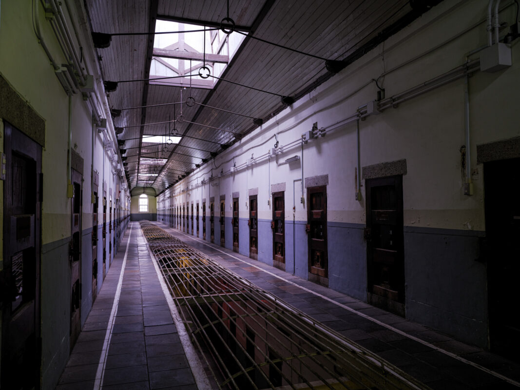 Empty Nara Prison corridor with skylight, tiled floor, and heavy cell doors on both sides