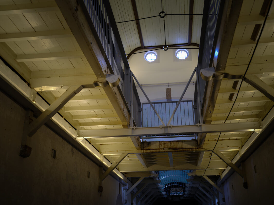 Upward view of Nara Prison interior, stacked walkways and circular windows in dim light.