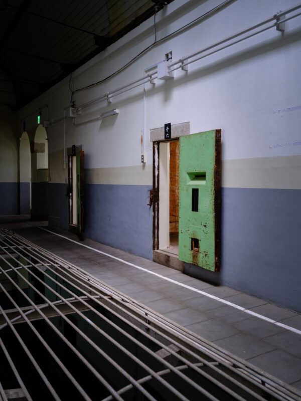 Eerie Nara Prison corridor with rusted cell doors, exposed pipes, and steel grate floor.