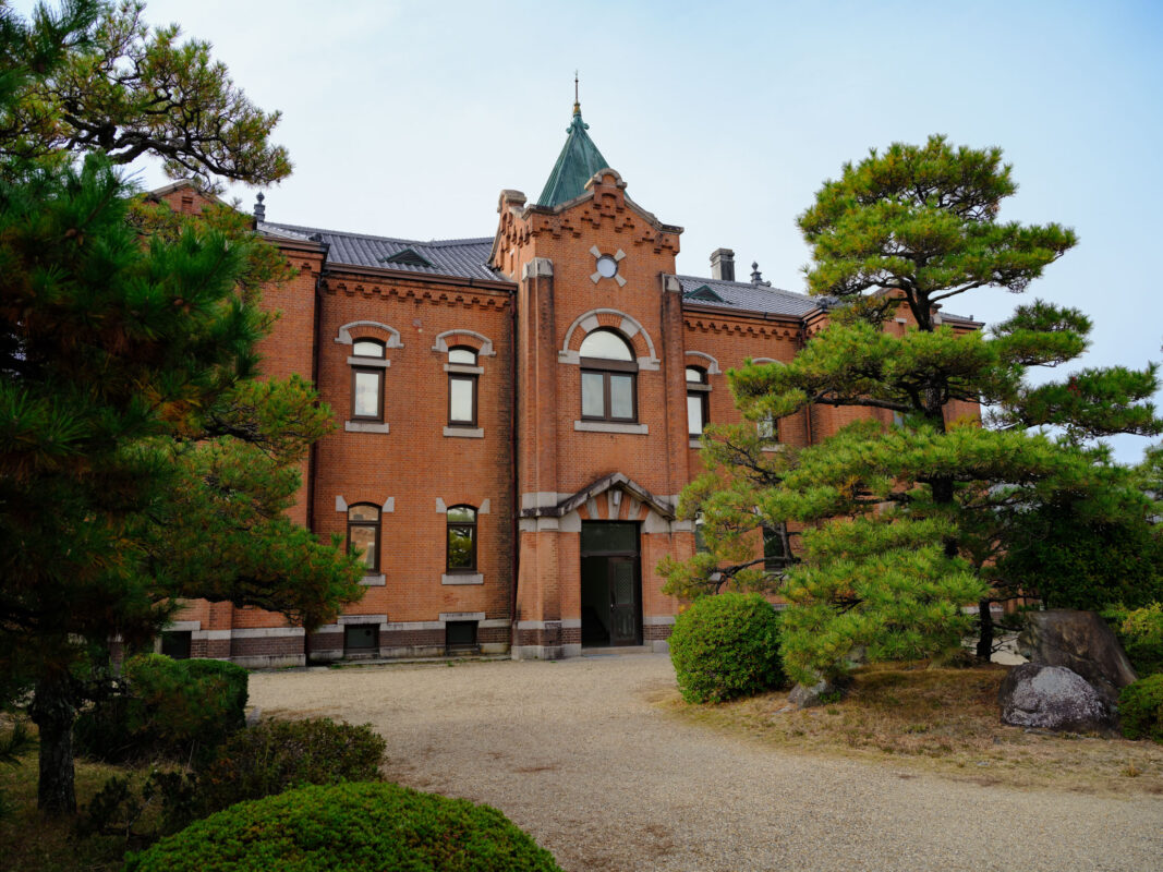 Historic Nara Prison red-brick facade with arched windows, gabled entrance, and landscaped pines.