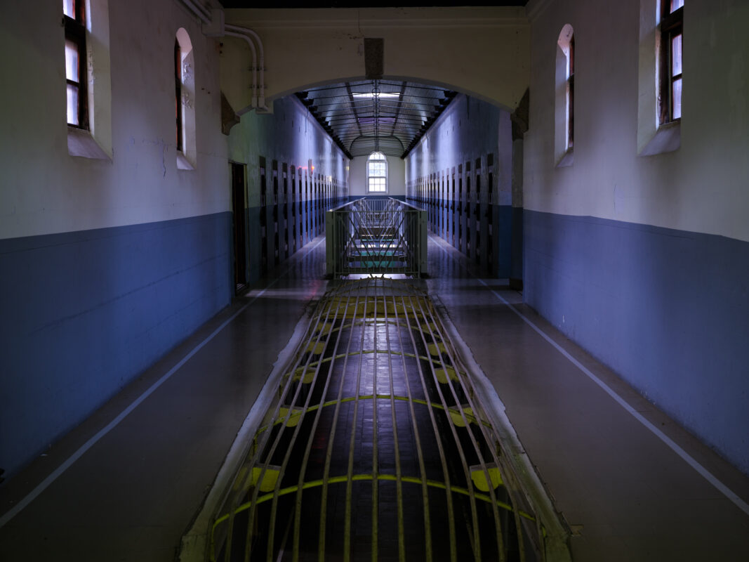 Symmetrical corridor inside Nara Prison with cell doors, blue-white walls, and central metal grate