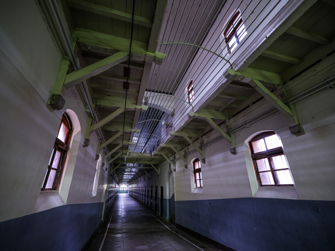 Symmetrical corridor inside Nara Prison with arched windows and green beams, eerie light.