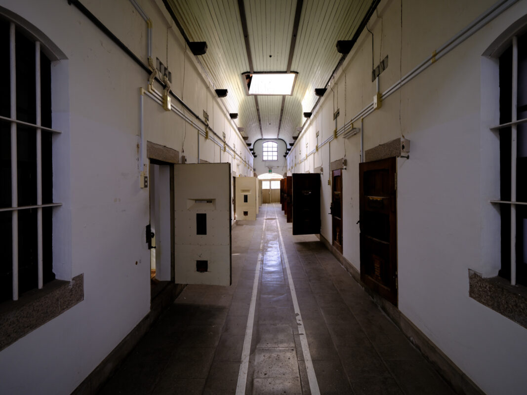 Symmetrical corridor in historic Nara Prison, lined with cell doors and arched ceiling lights.
