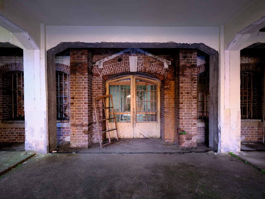 Abandoned Nara Prison entrance with weathered wooden double doors, brick arch, and ladder