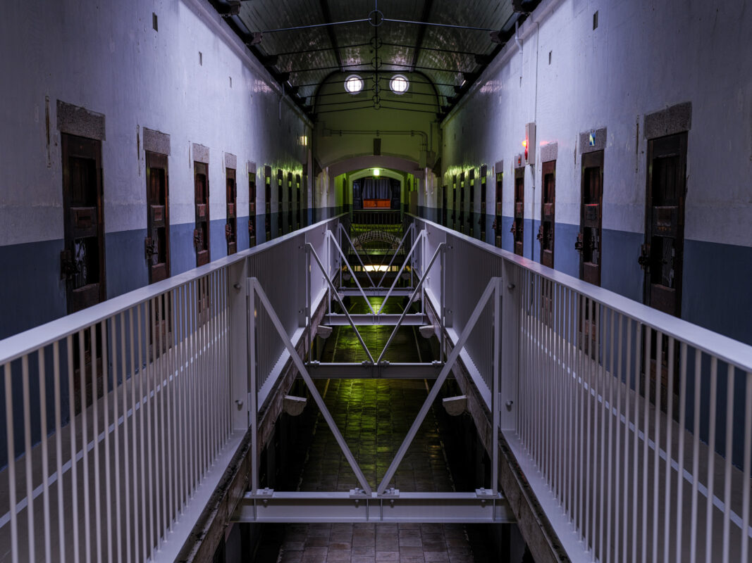Symmetrical Nara Prison cell block corridor with metal walkway, barred doors, and arched ceiling