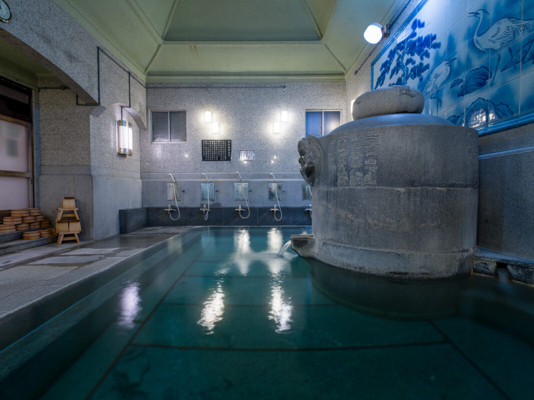 Interior of Dogo Onsen hot spring bath with tiled pool, washing stations, and mural