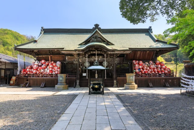 Crimson dreams whisper, Wooden echoes of the past, In tranquil embrace.  赤夢囁く、 過去の木の響き、 静かな抱擁。  #DarumaDreams #ShrineQuietude #SereneJapan #RuralRetreat #CulturalSymbols #offbeatjapan #japan