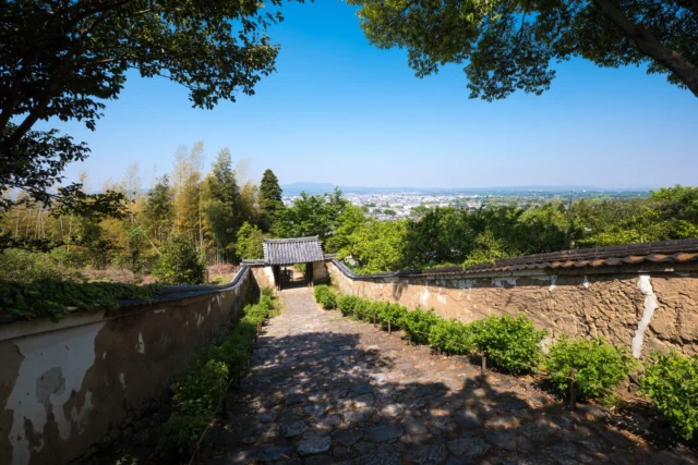 Worn stones tell stories, Ancient gate meets cityscape— Tradition whispers. 石畳 古門で都市会う 伝統囁く #offbeatjapan #japan #traditionandmodernity #cityscape #serenity #ancientarchitecture #urbanblend