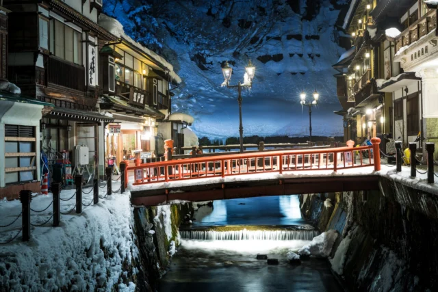 Red bridge spans the stream, Golden glimmers in the night, Winter whispers glow. ---赤い橋が流れる小川を渡り、 金色の輝きが夜を照らす、 冬の囁きが輝く。---#offbeatjapan #japan #winterwonderland #traditionallife #serenenight #onsenvibes #redbridge